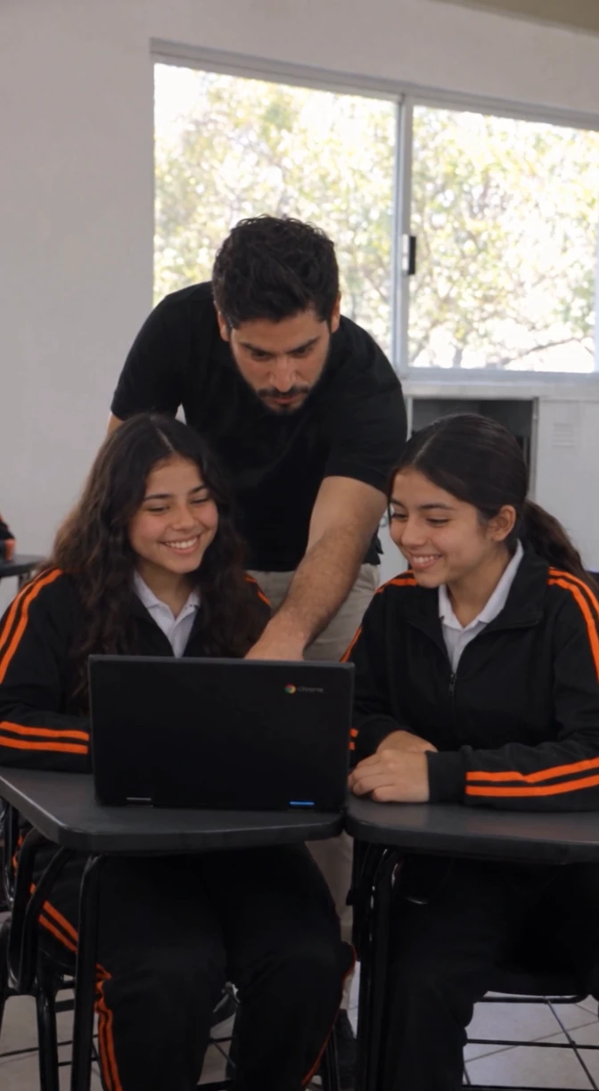 Un docente acompaña a dos estudiantes mientras trabajan en una Chromebook